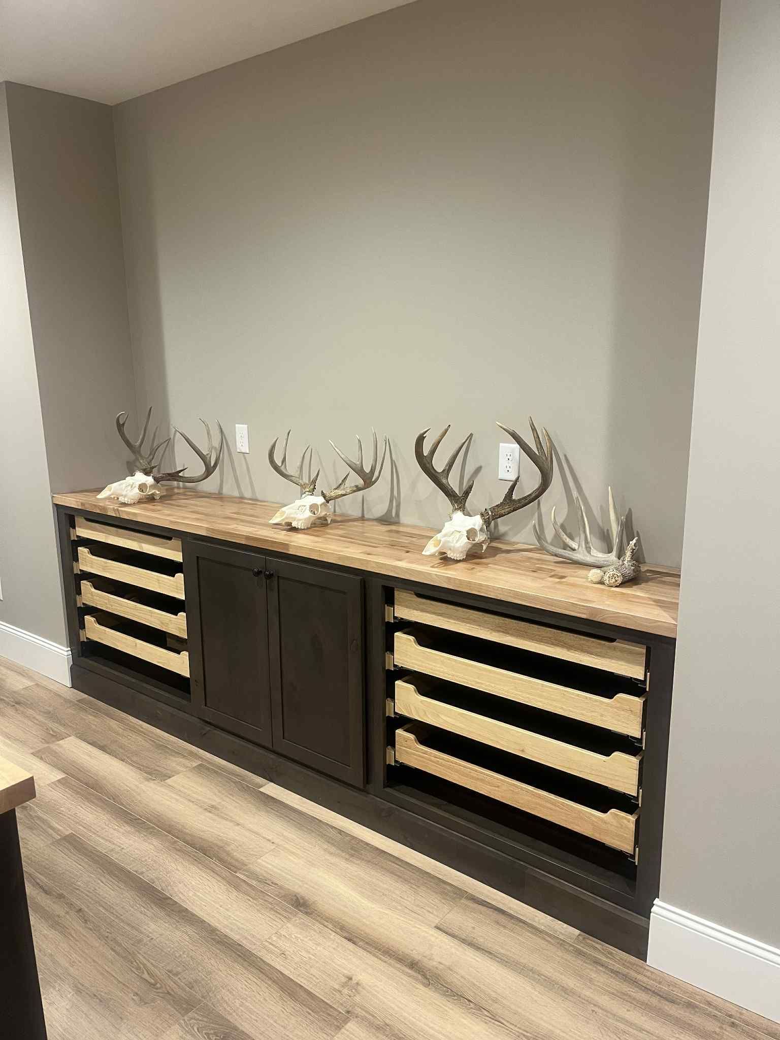 Cabinet with animal skulls and antlers on a wooden countertop, set against a gray wall and light flooring.