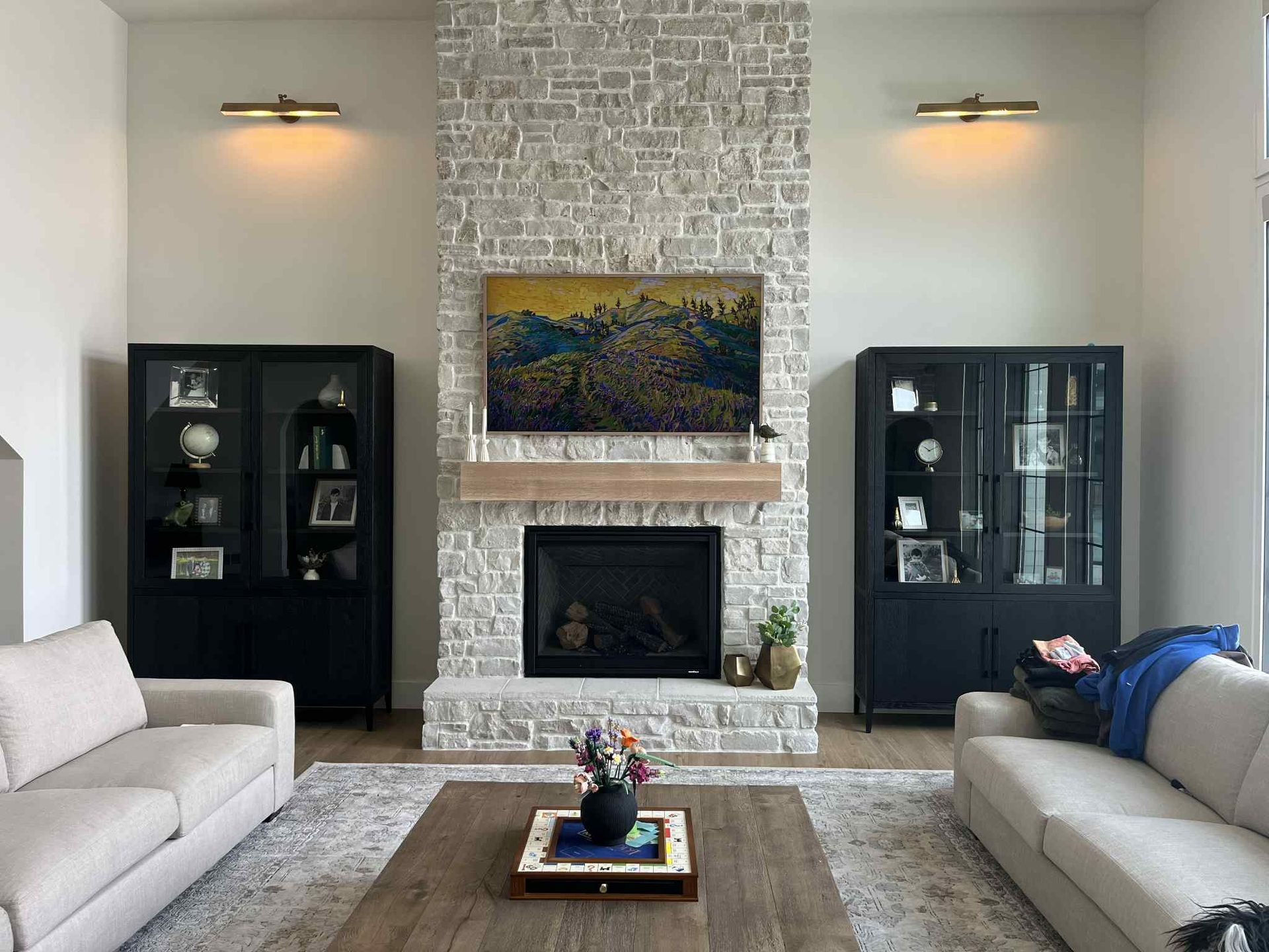 Living room with stone fireplace, flanked by black cabinets, and two cream-colored sofas.