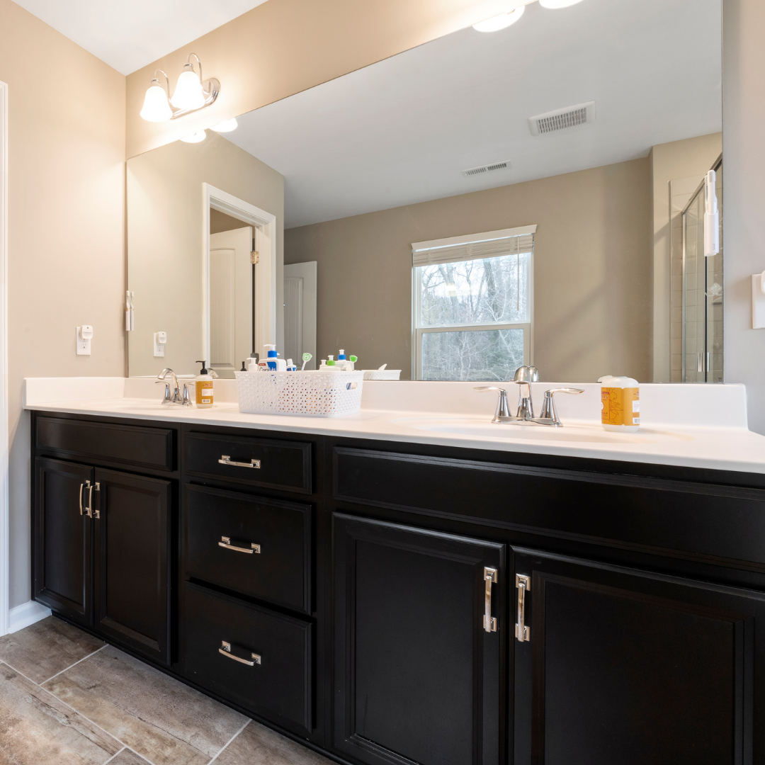 Bathroom with black cabinets, white countertop, large mirror, and beige walls.