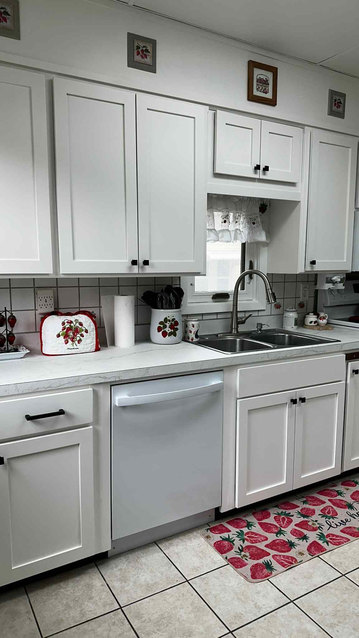White kitchen cabinets with a stainless steel dishwasher and sink, floral rug.