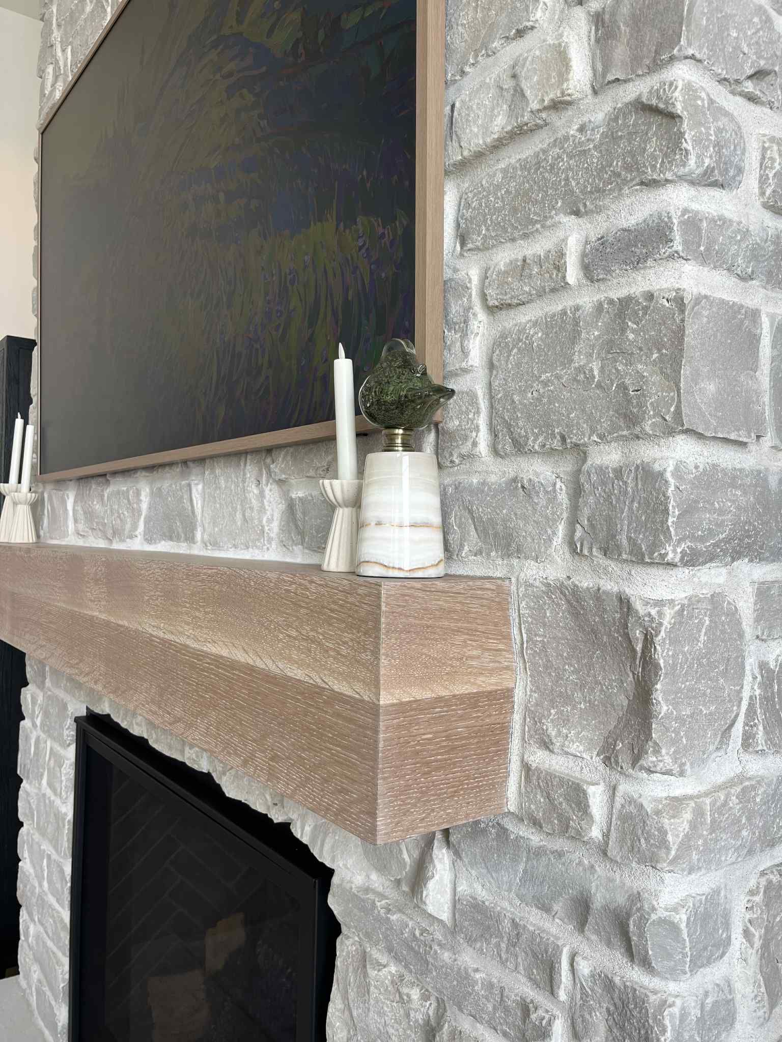 Stone fireplace with a wooden mantle. A painting and candles sit above the fireplace opening.