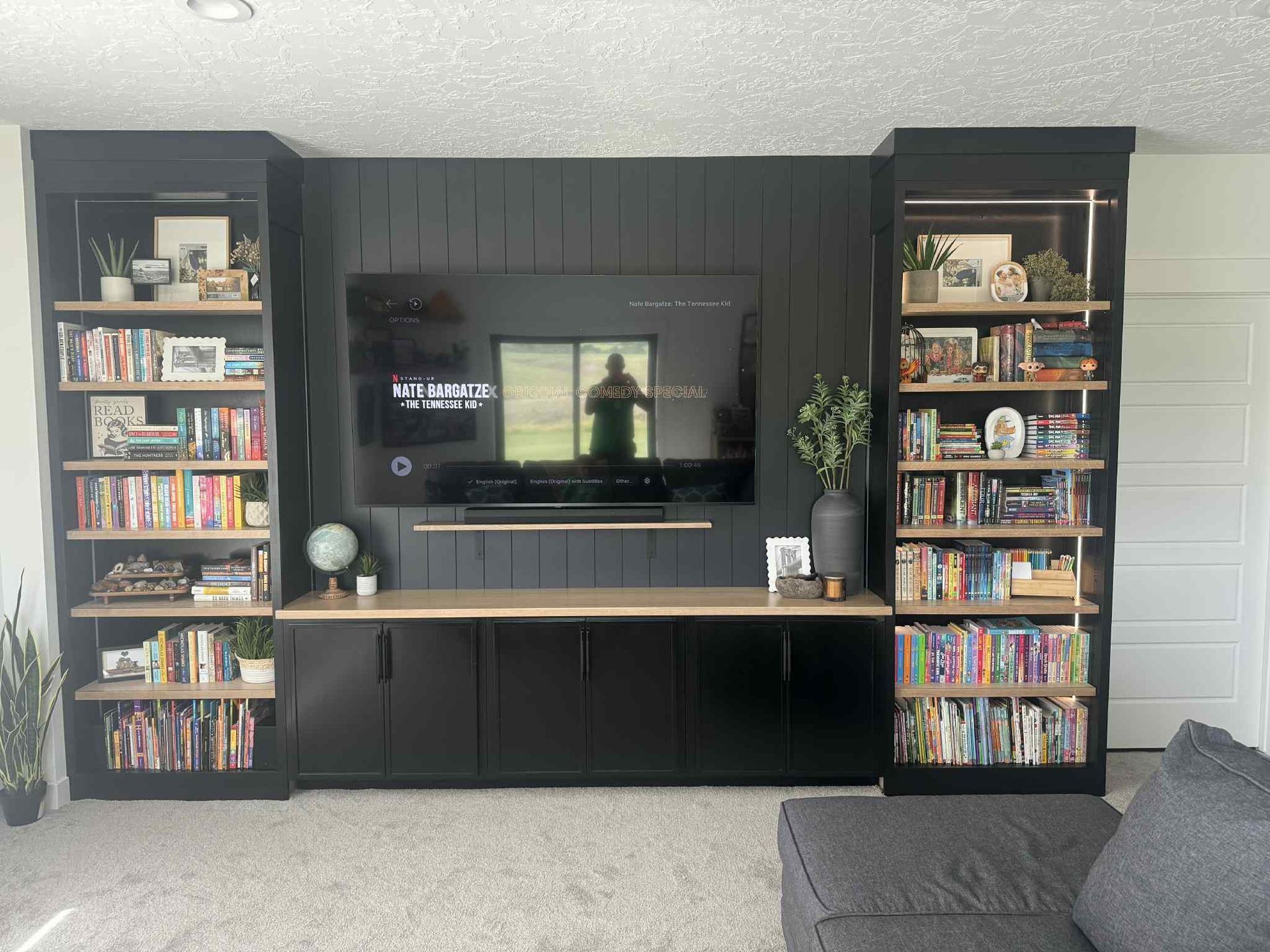 Black entertainment center with a TV, cabinets, and bookshelves, against a black shiplap wall.
