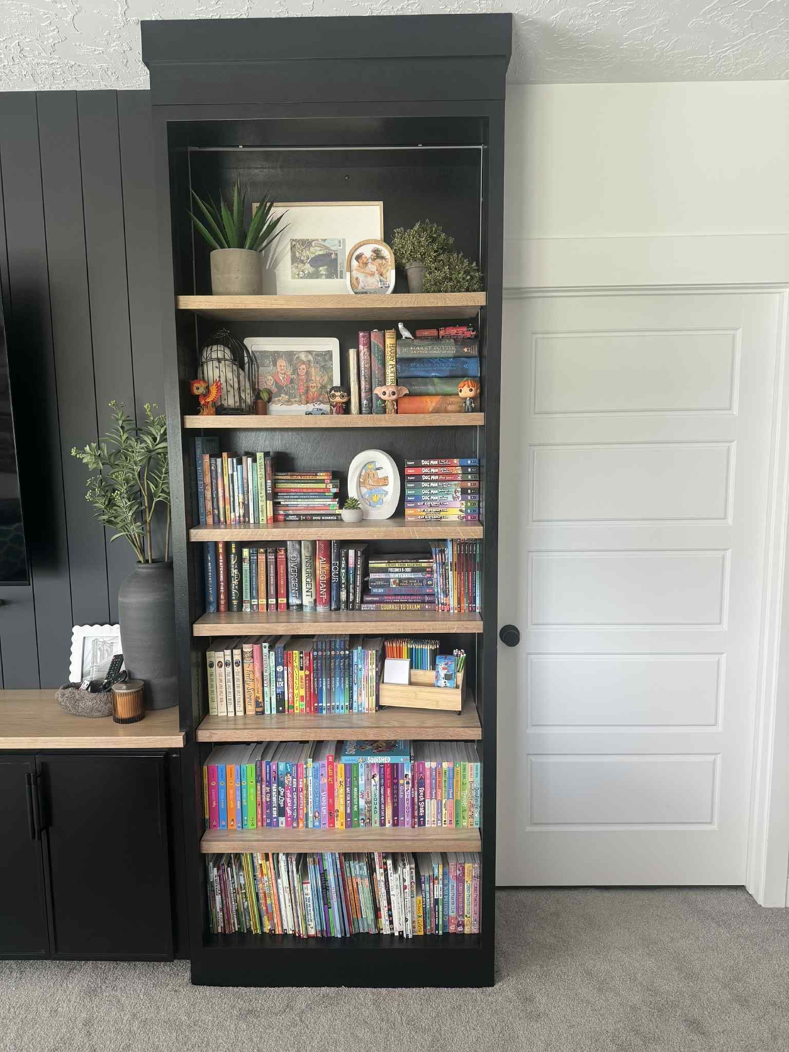 Tall black bookshelf with wood shelves, filled with books and decorative items, next to a white door.