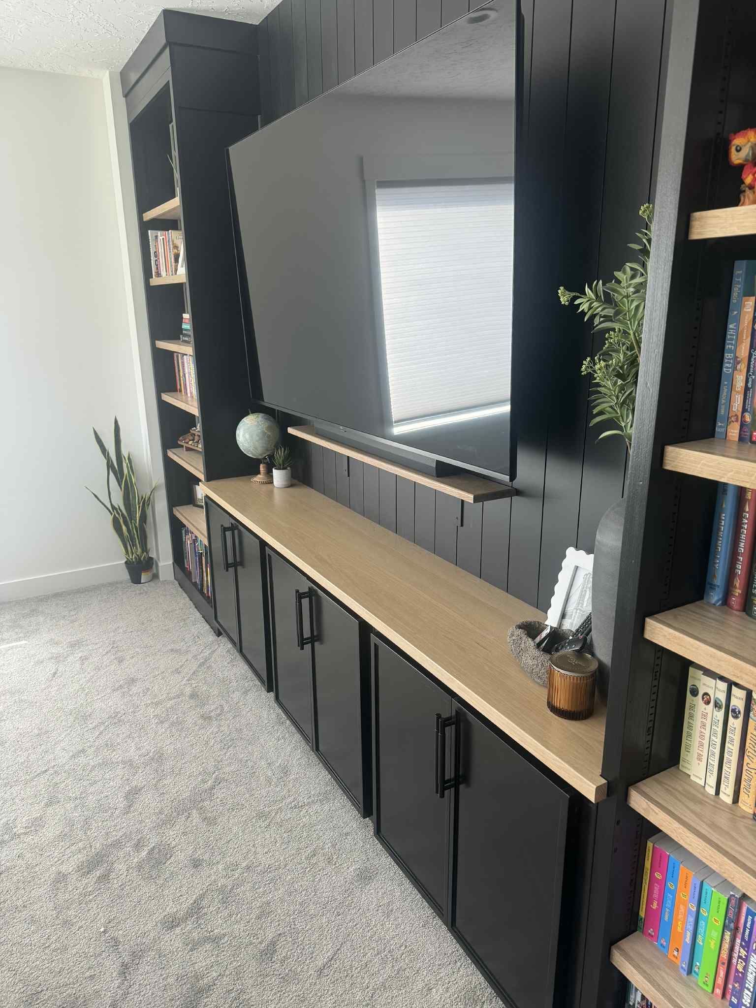 Black built-in entertainment center with TV, cabinetry, shelving, and wooden countertop in room with neutral carpet.