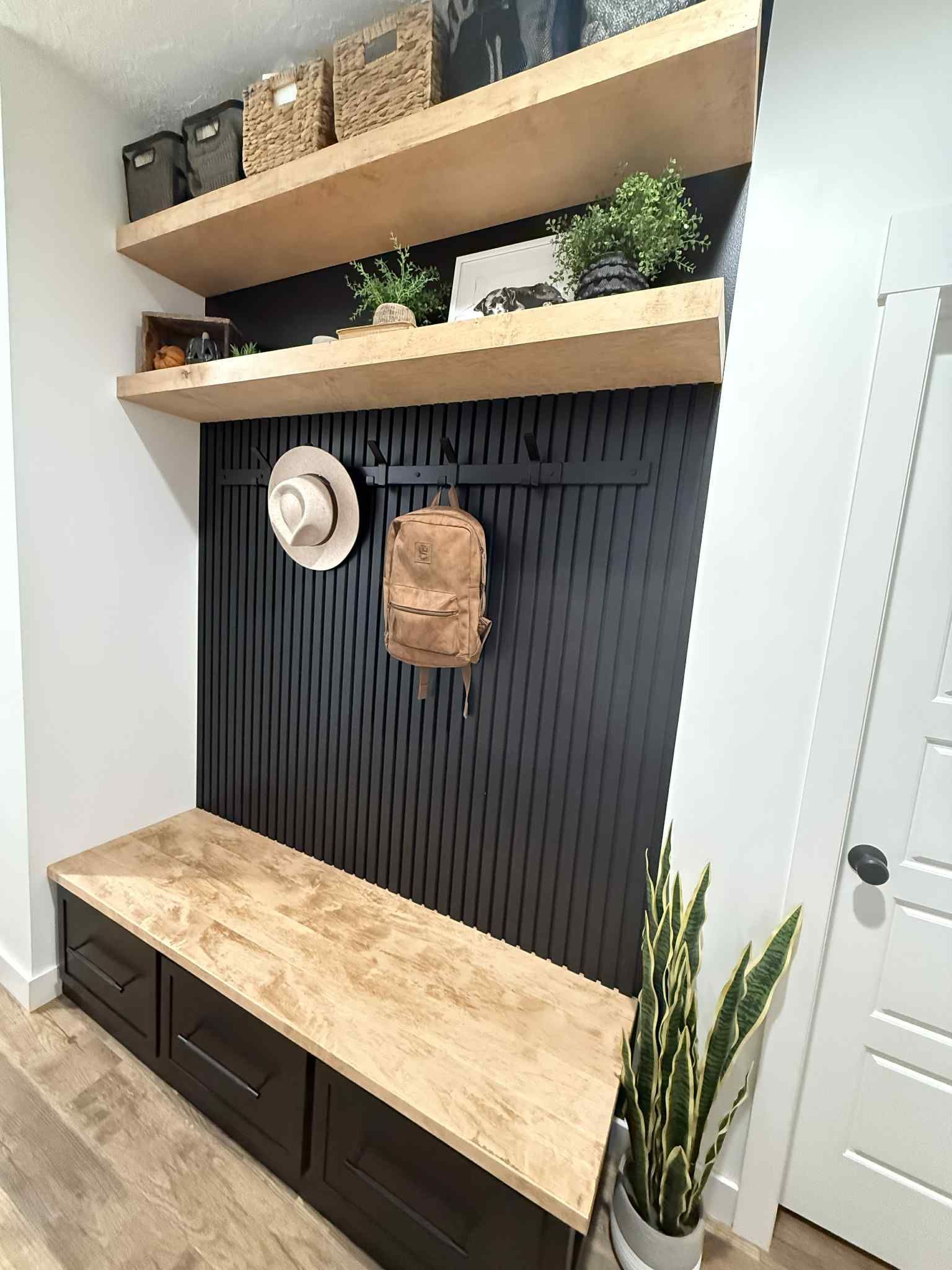 Mudroom with black paneling, wooden shelves, and a bench; plants and storage baskets.