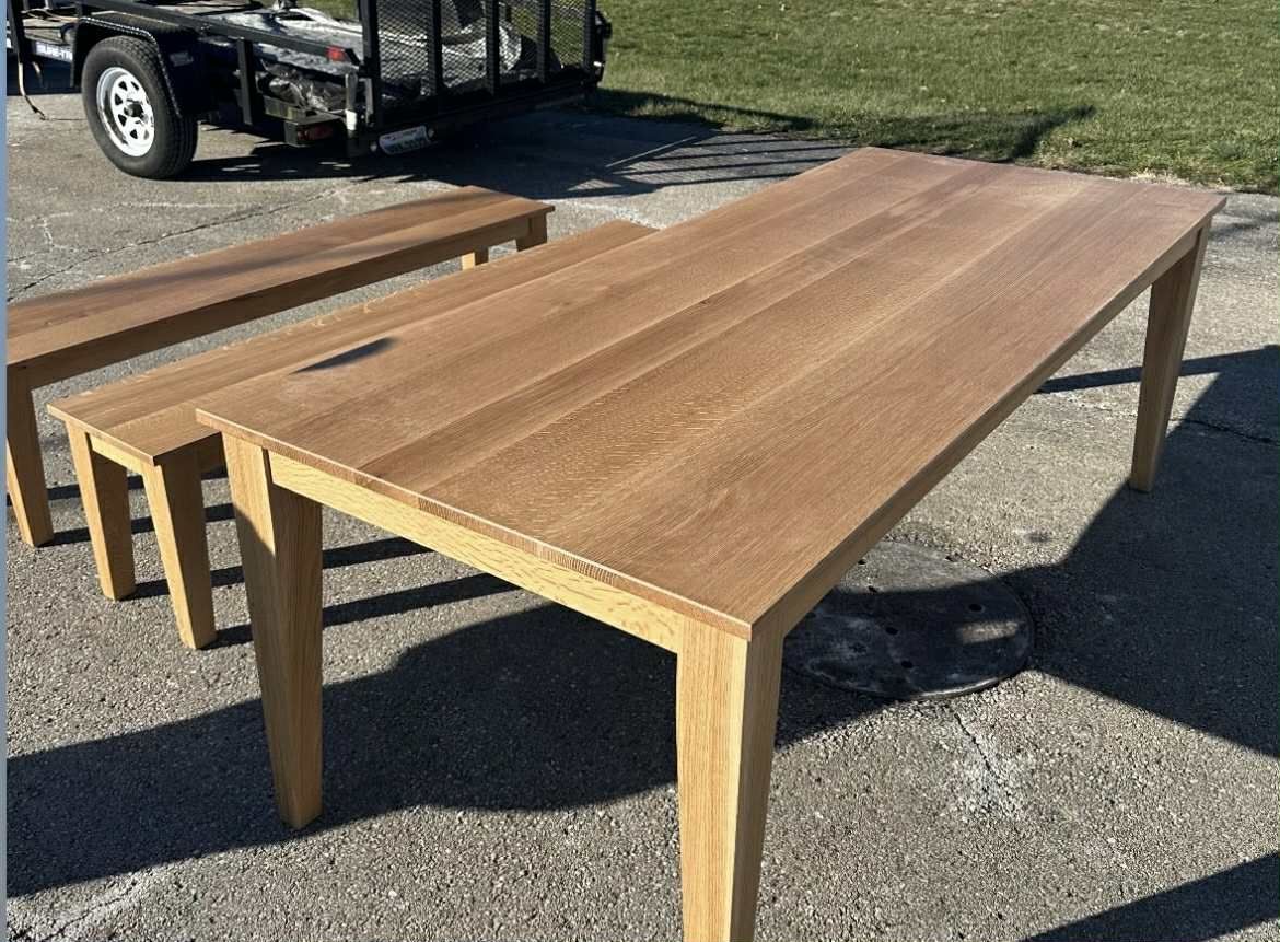 Wooden table and bench set on a paved surface, with a trailer in the background.