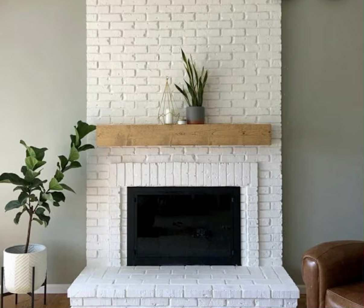 White brick fireplace with a wood mantle, house plants, and a black fireplace insert.