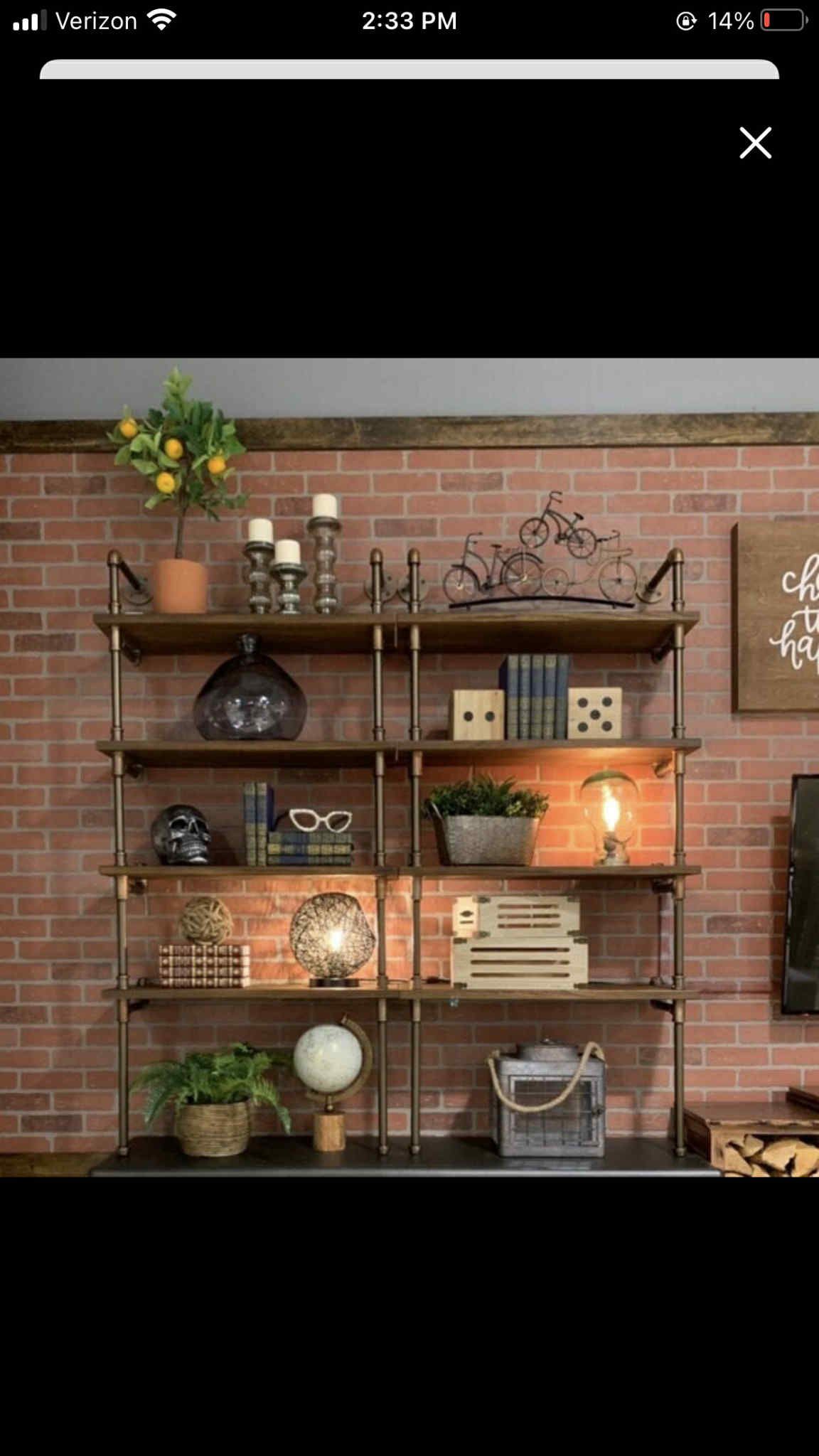 Shelving unit with wood shelves, brass piping, and various decorations in front of a brick wall.