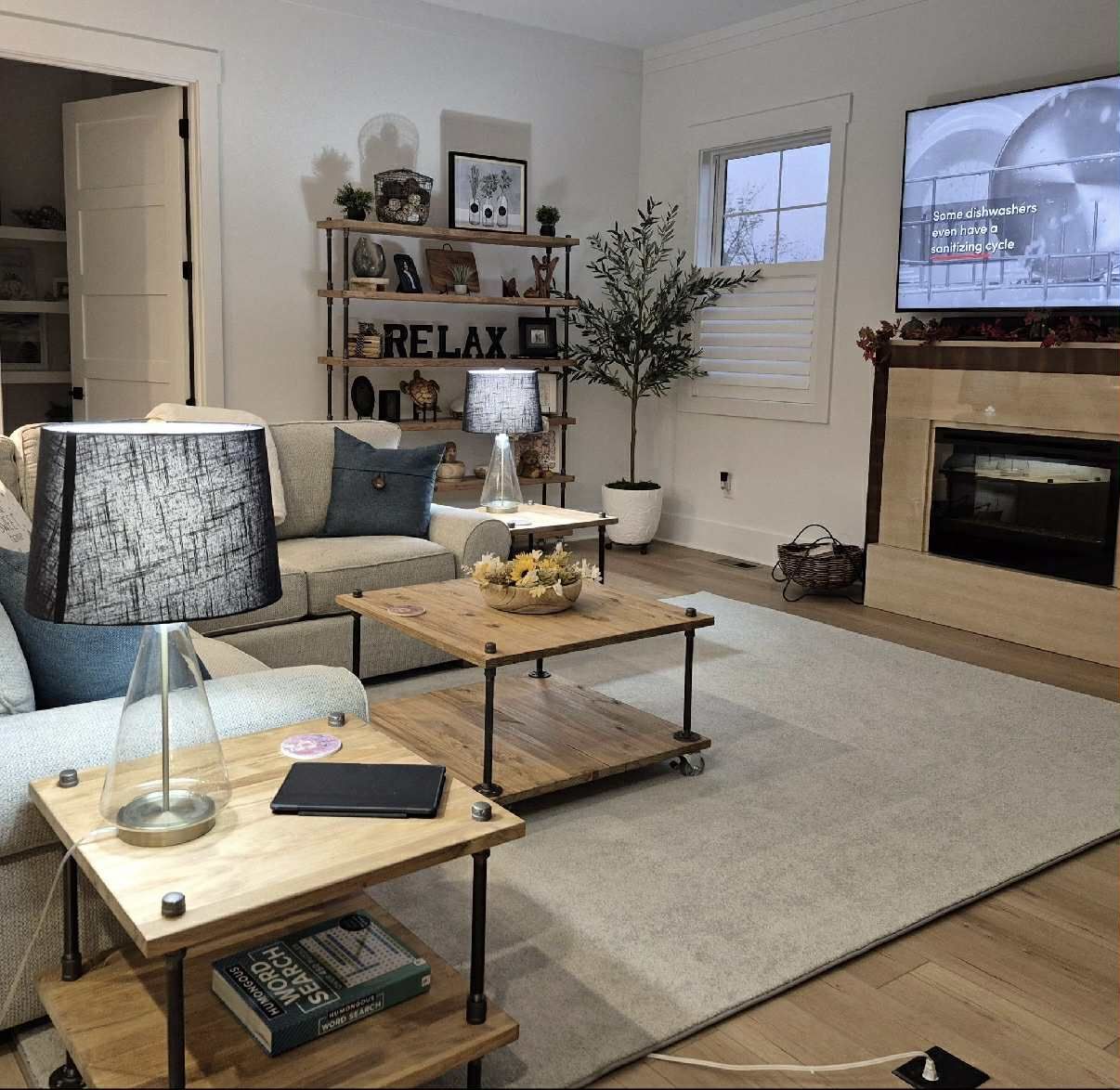 Cozy living room with fireplace, TV, couch, and wooden tables with decorative items and plants.