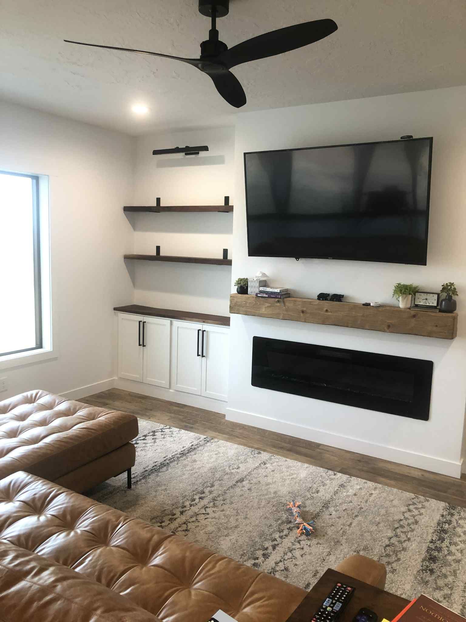 Living room with TV, fireplace, floating shelves, and brown leather sectional.