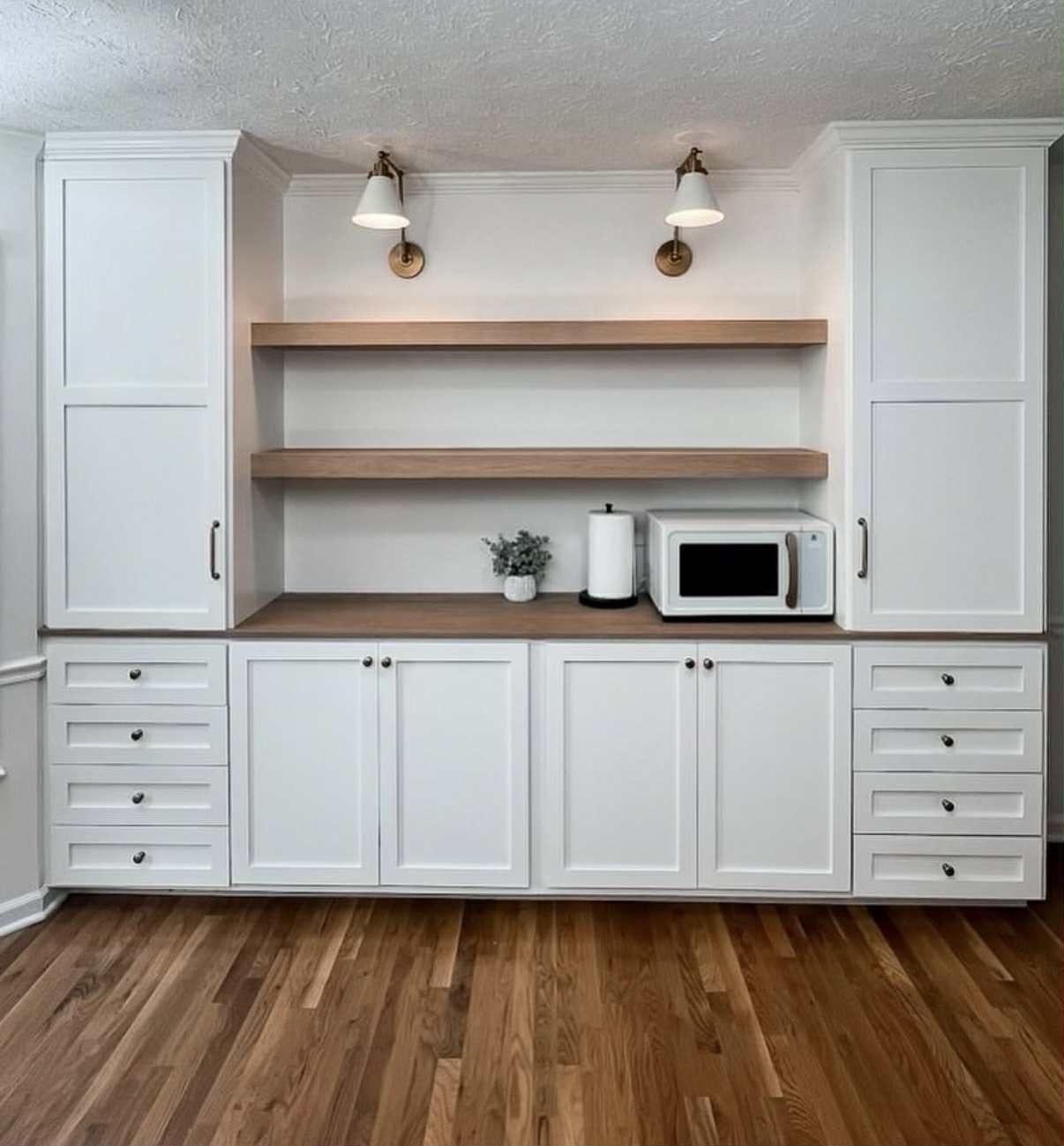 Built-in white cabinets with a countertop, shelves, and a microwave in a kitchen nook with hardwood flooring.