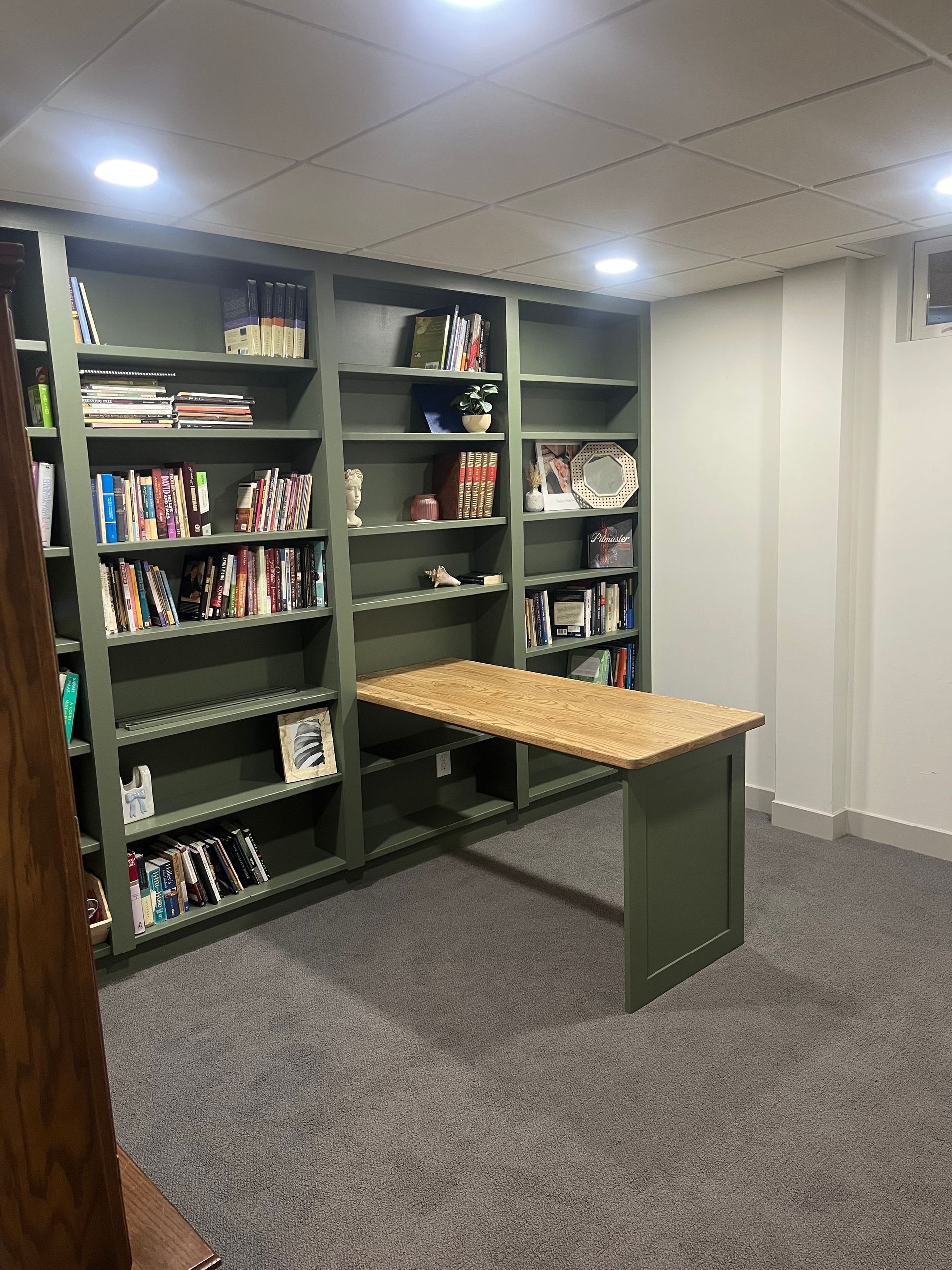 Green built-in bookshelves with a fold-down desk. Books and objects on shelves; room with gray carpet and white walls.