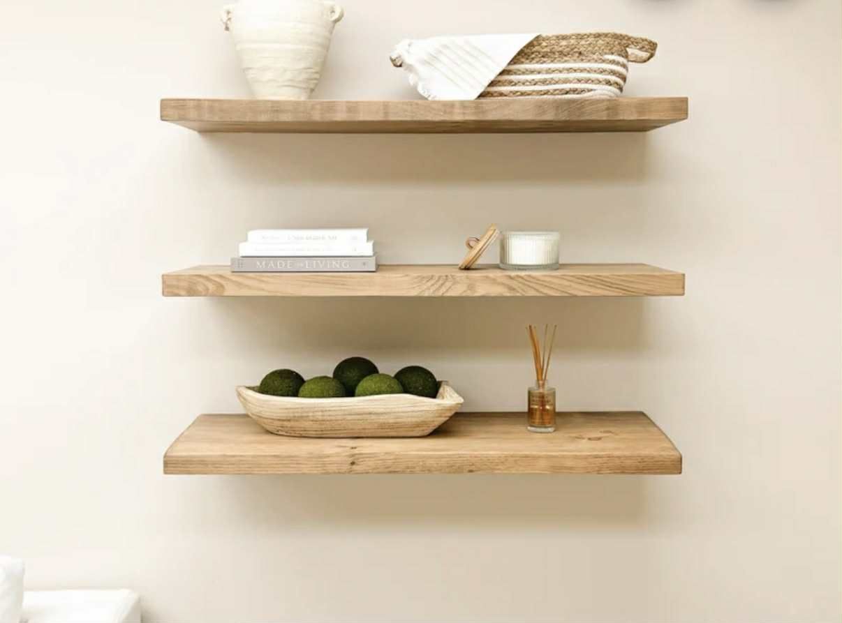 Three wooden floating shelves on a beige wall, displaying decor items.