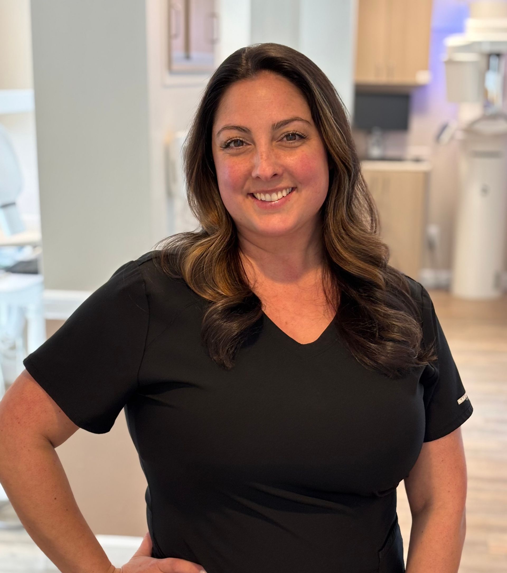 Woman in black scrubs smiles at the camera, standing in a dental office.