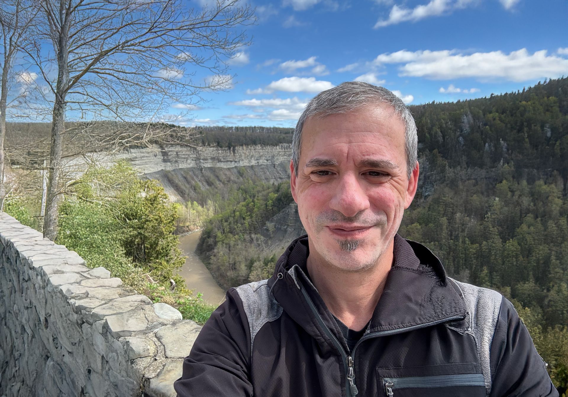 Person standing on a hilltop, silhouetted against the sunset over mountain range, grassy field.