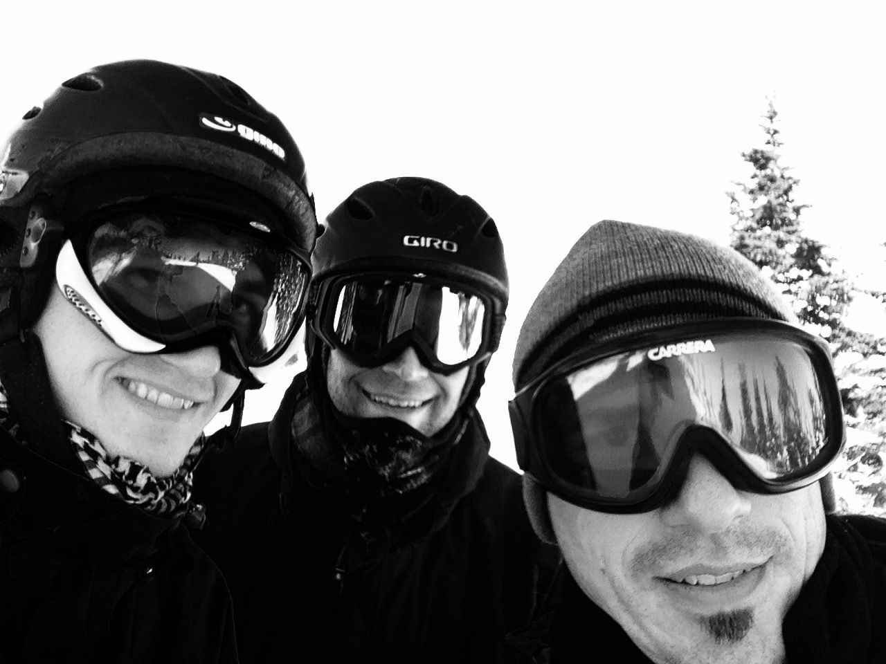Three people in ski gear smiling, snowy mountain background.