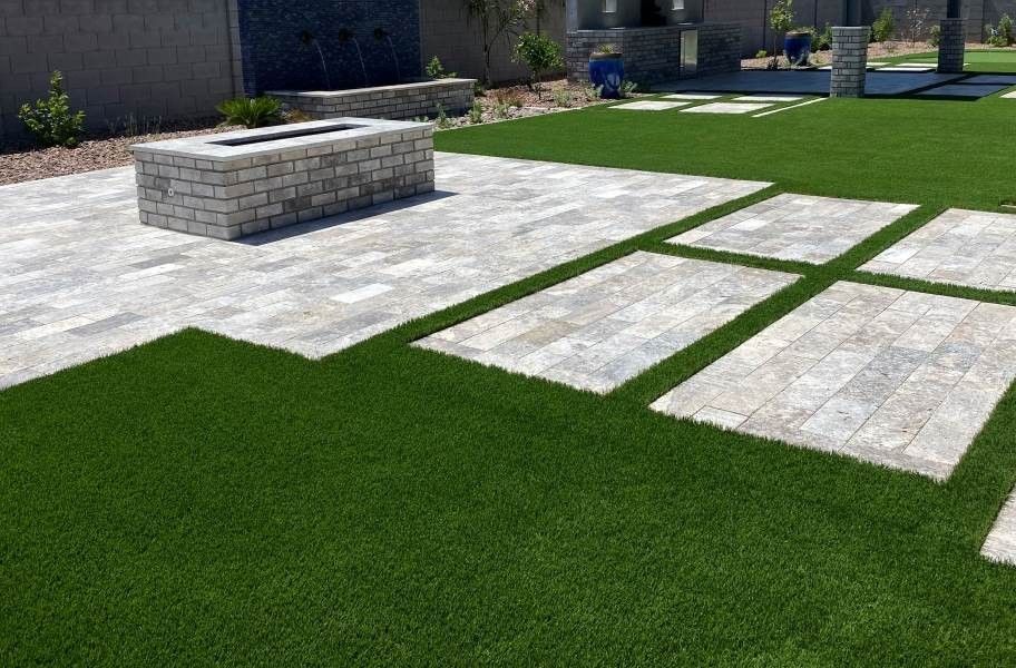 Patio with stone pavers and a rectangular fire pit surrounded by artificial green grass.