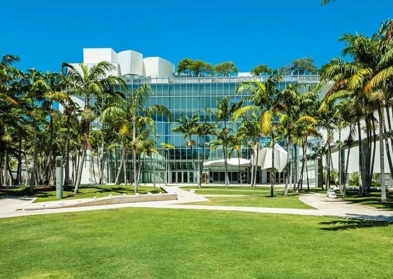 Modern art museum with palm trees and green lawn under a bright blue sky.