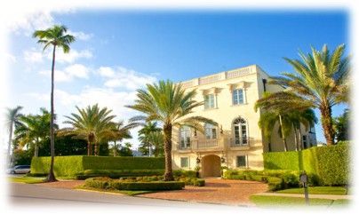 Elegant beige mansion surrounded by palm trees and manicured hedges on a sunny day.