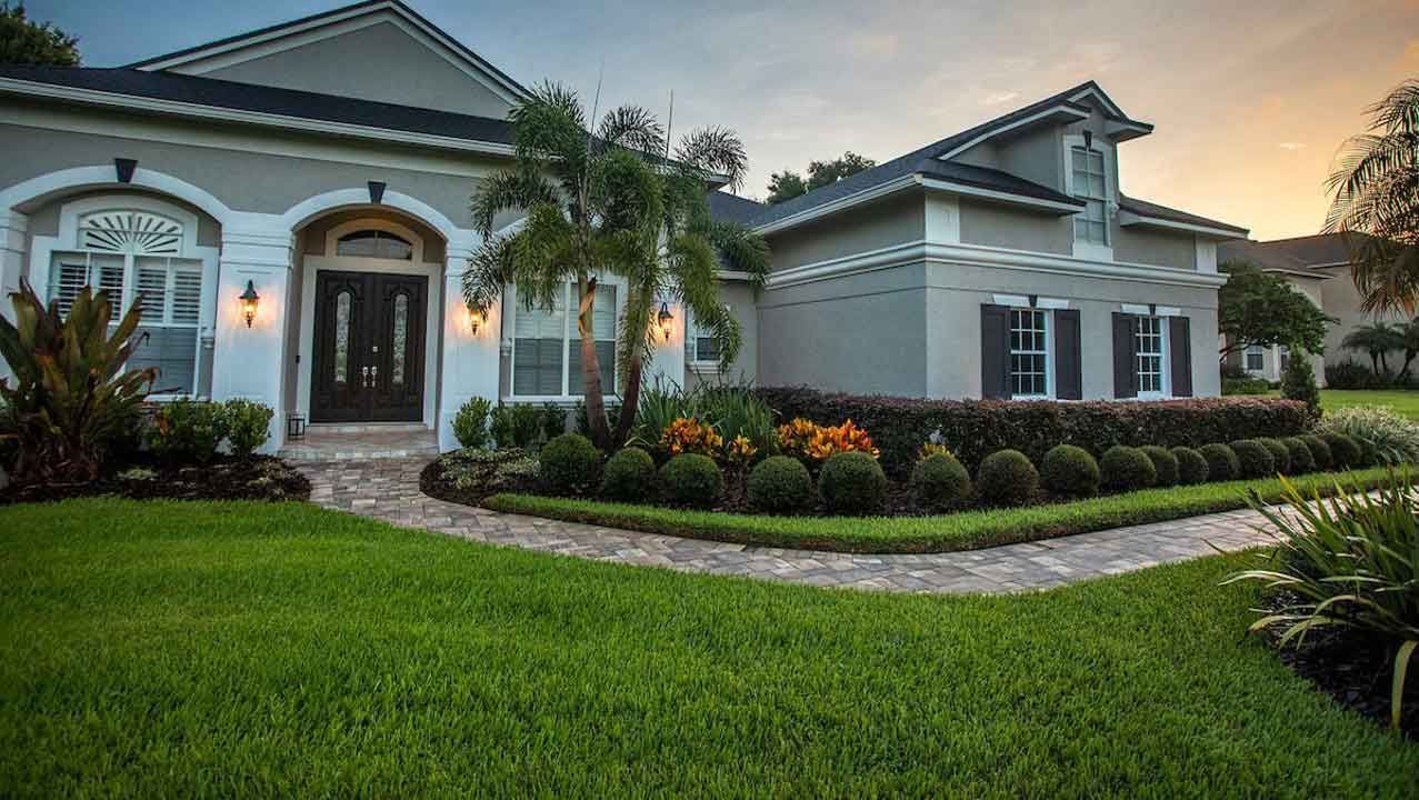 Suburban home with manicured lawn and garden beds, gray exterior, front door and windows.