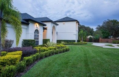 White house with manicured lawn and shrubs, under a cloudy sky.