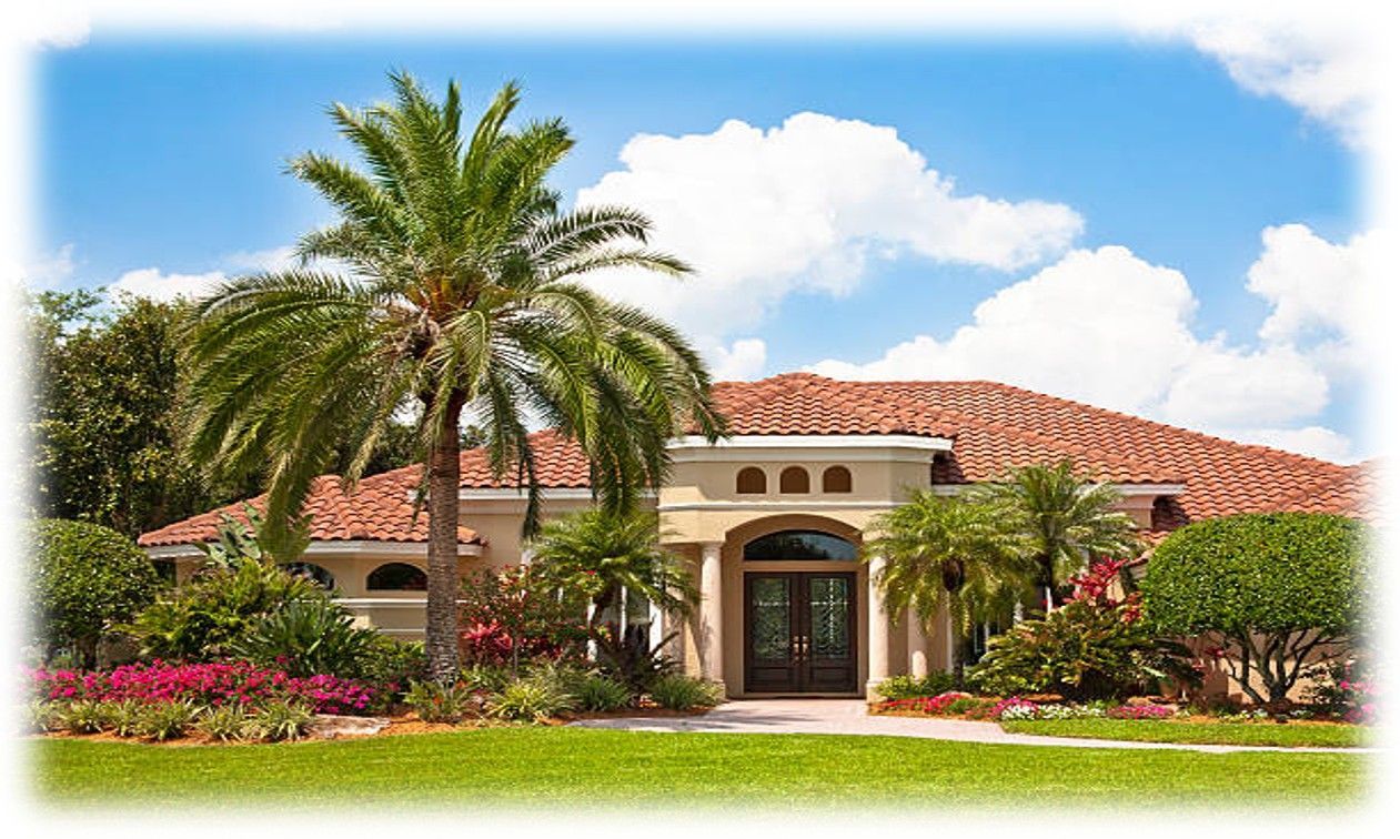 Tropical home with palm trees, red-tiled roof, and lush landscaping against a bright blue sky.