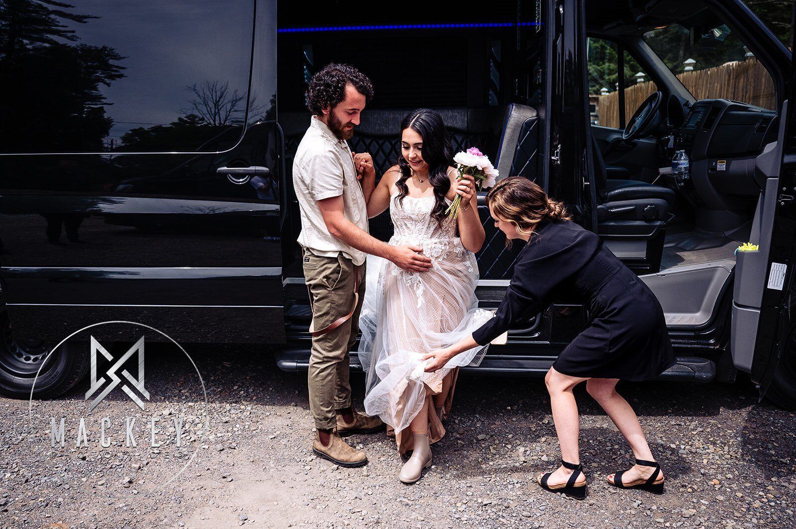 A bride and groom are standing next to a black van.