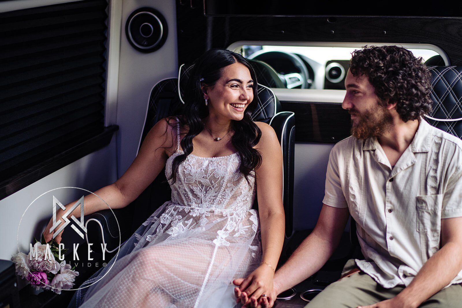 A bride and groom are sitting in a limousine holding hands.