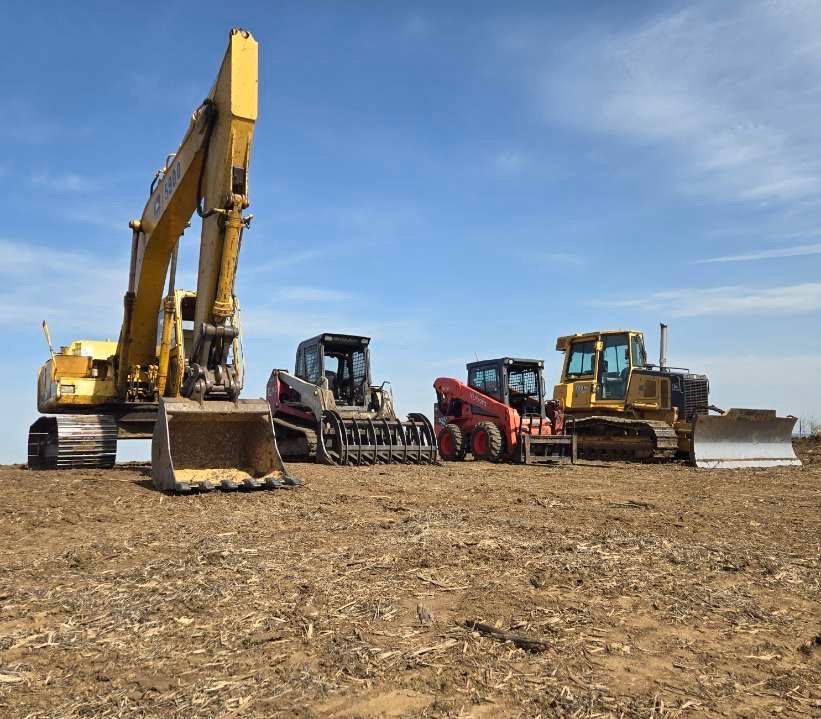 A group of construction vehicles are parked in a dirt field.
