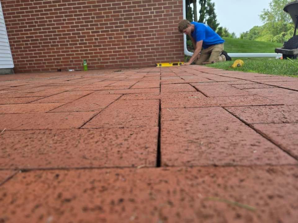 A man is kneeling down on a brick driveway.