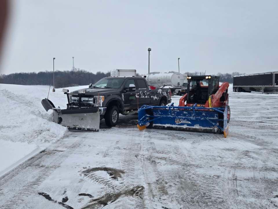 Two snow plows are parked next to each other in a parking lot.