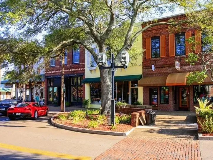 A red car is parked in front of a row of buildings.