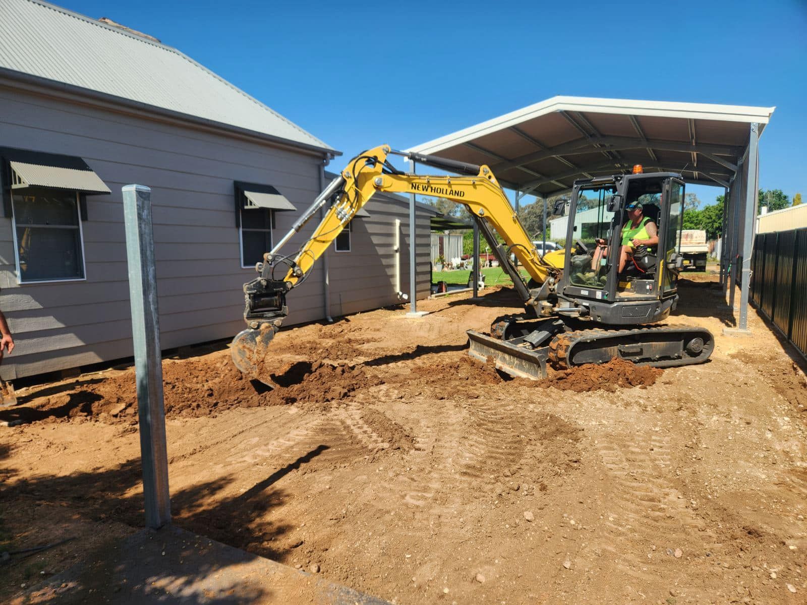 A yellow excavator is digging a hole in the dirt in front of a house.
