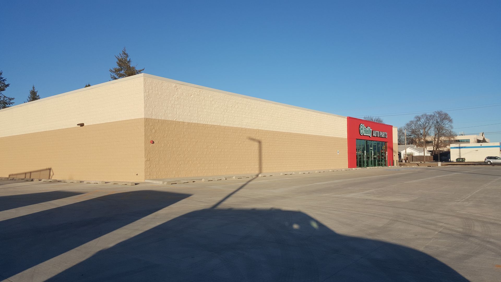 Exterior of a tan and cream-colored commercial building with a red and green entrance, set against a blue sky.