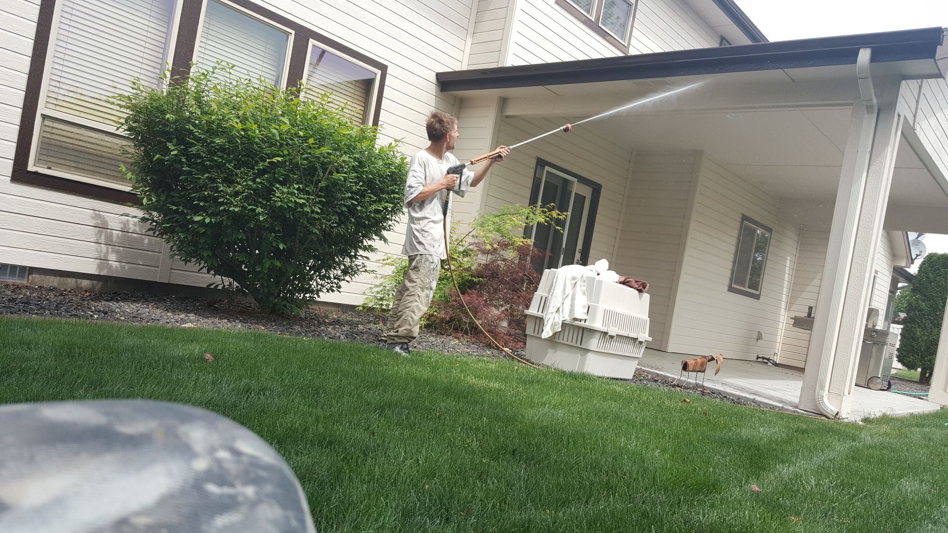 Person painting the exterior of a house with a long roller, standing on a green lawn.