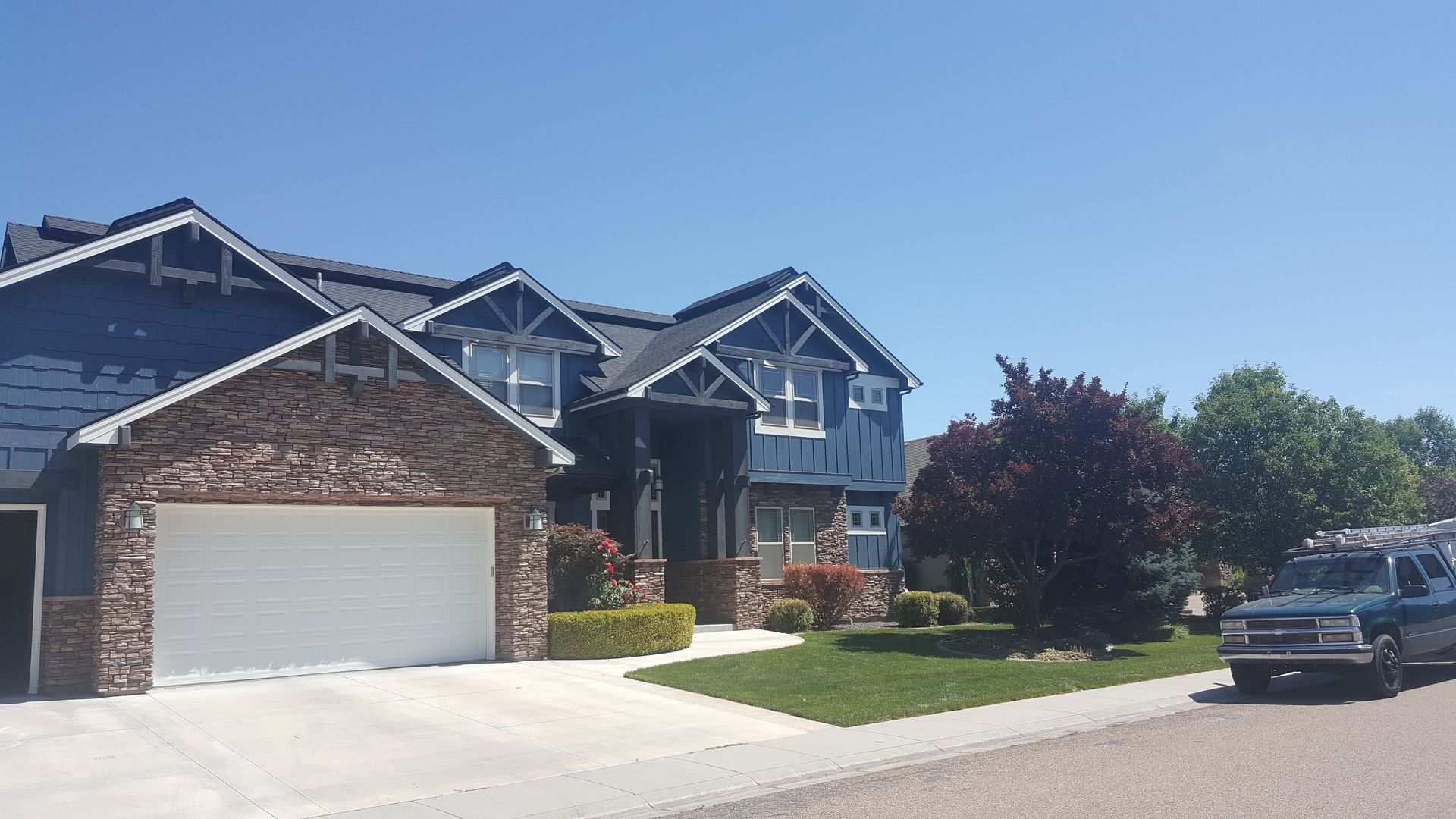 Two-story blue house with stone accents and a white garage door on a sunny day. A truck is parked on the side.
