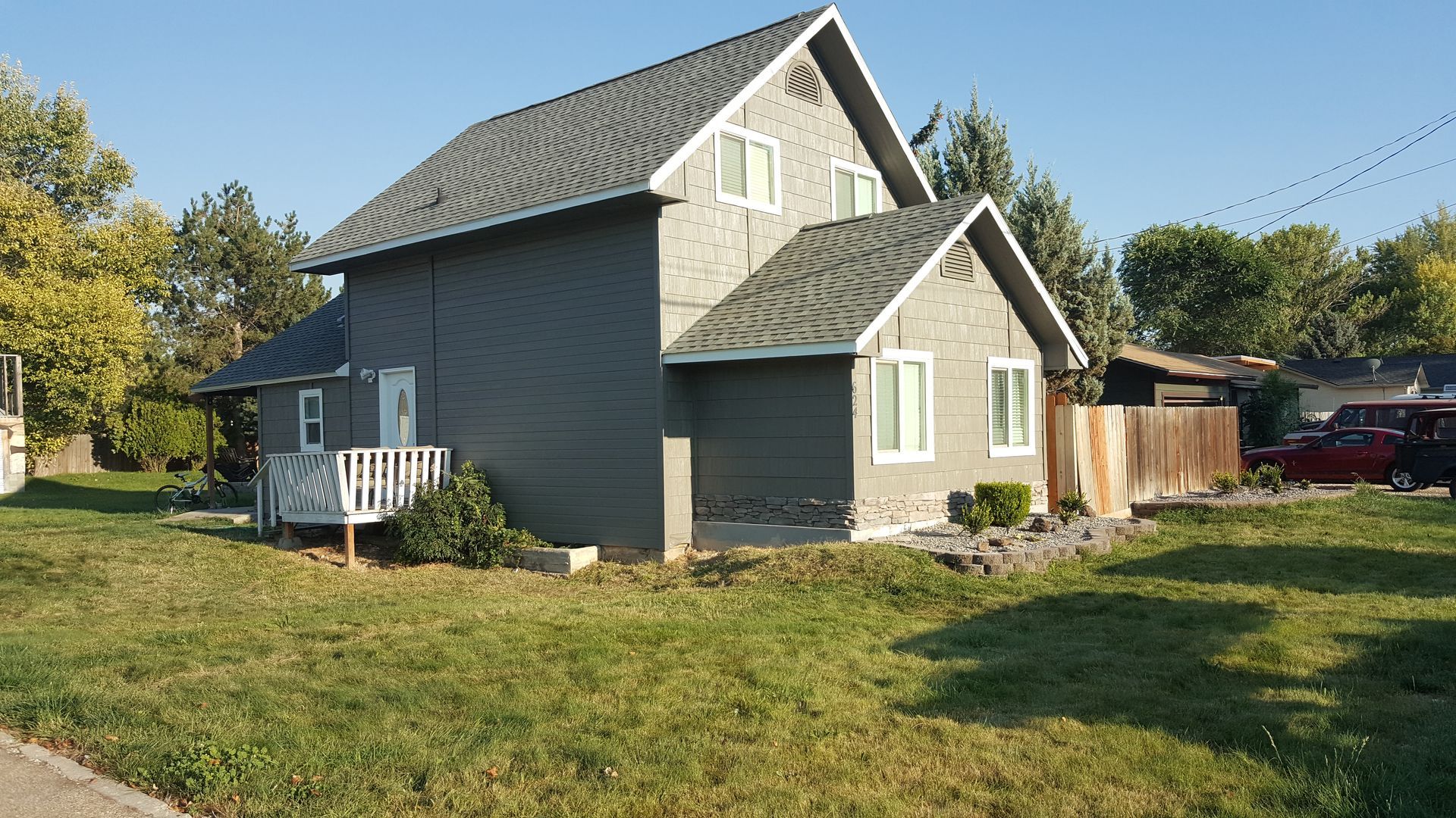 Gray two-story house with white trim, a small porch, and a grassy front yard on a sunny day.