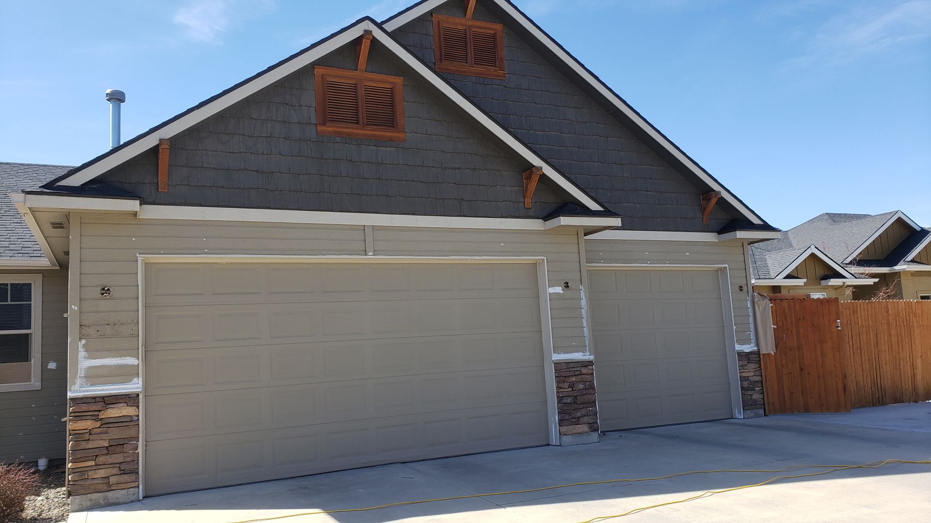 Two-car garage with grey doors and stone accents on a sunny day. The roof is dark grey with wooden detailing.