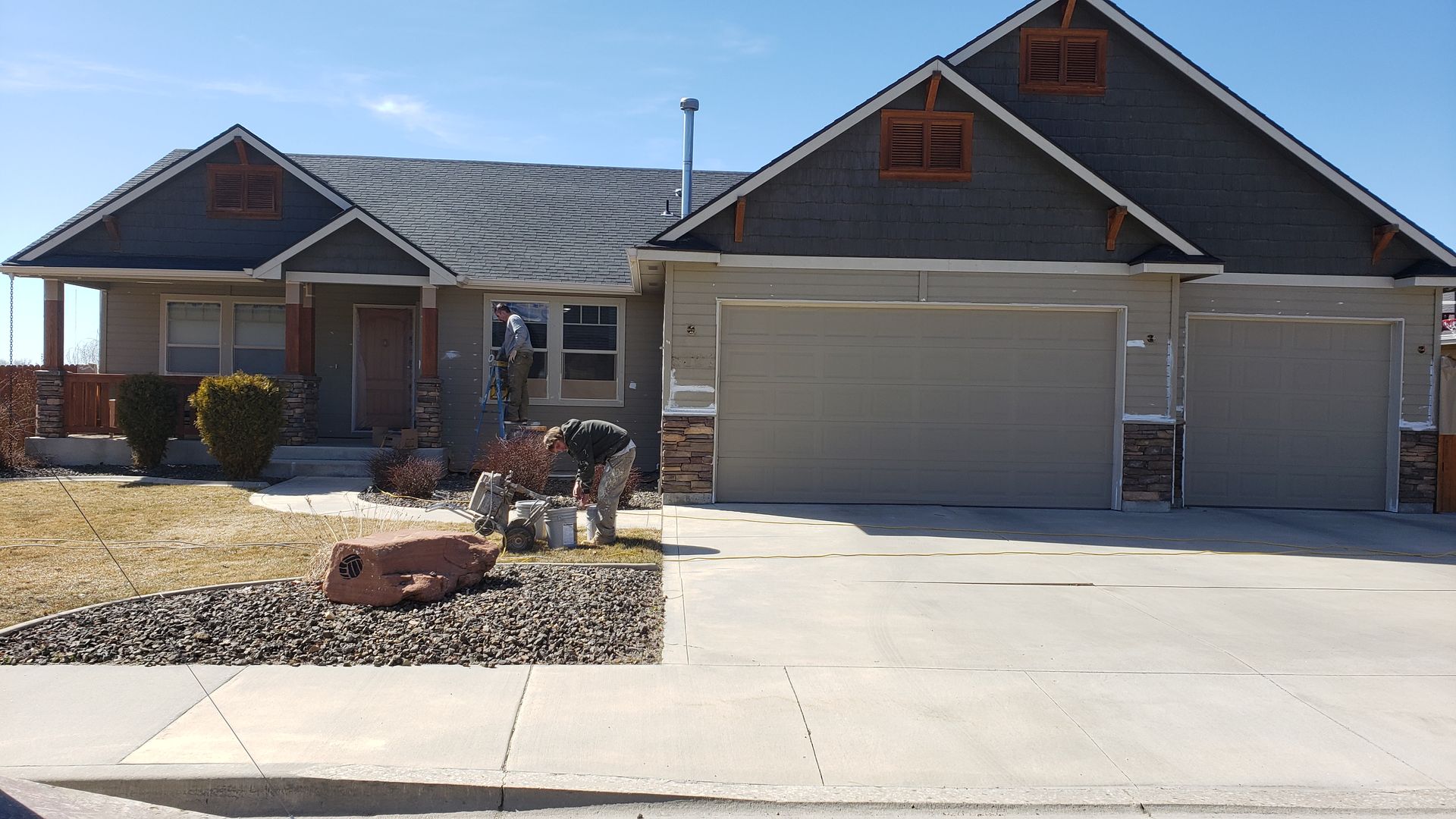 Beige house with a dark gray roof and two-car garage. A rock garden and driveway are in front.