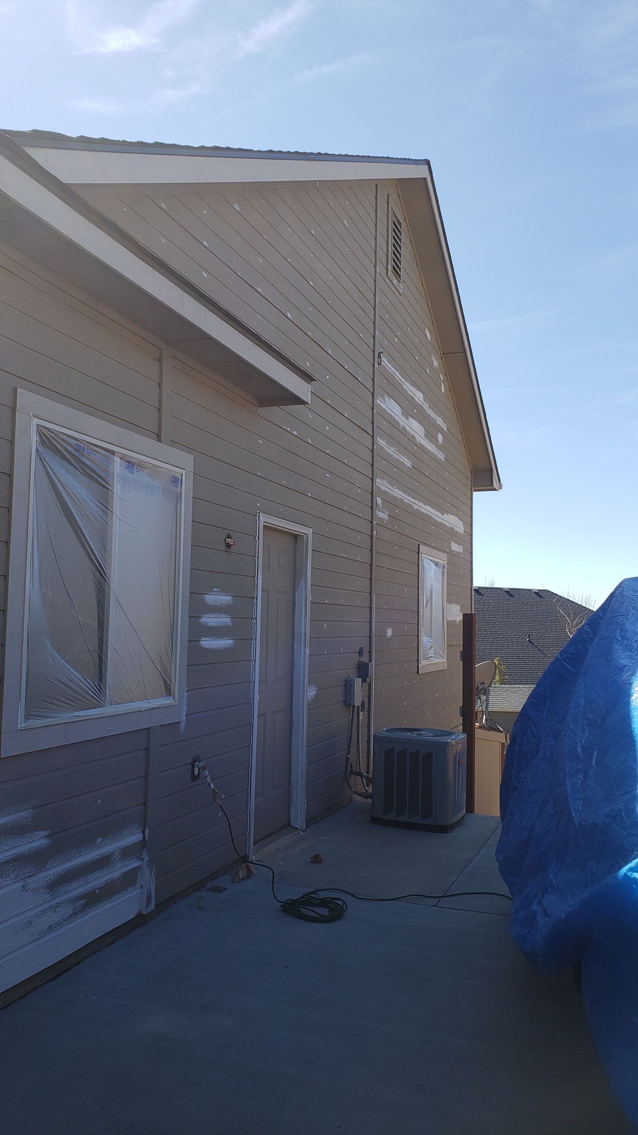 Exterior of a house under construction with exposed sheathing. The unfinished siding, doors, and windows are visible against a blue sky.