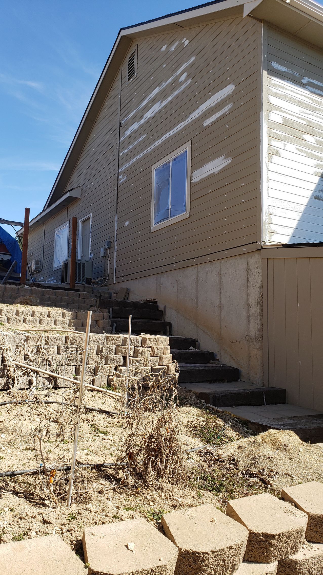 Side of a house with damaged siding and a concrete block staircase leading up from a yard.