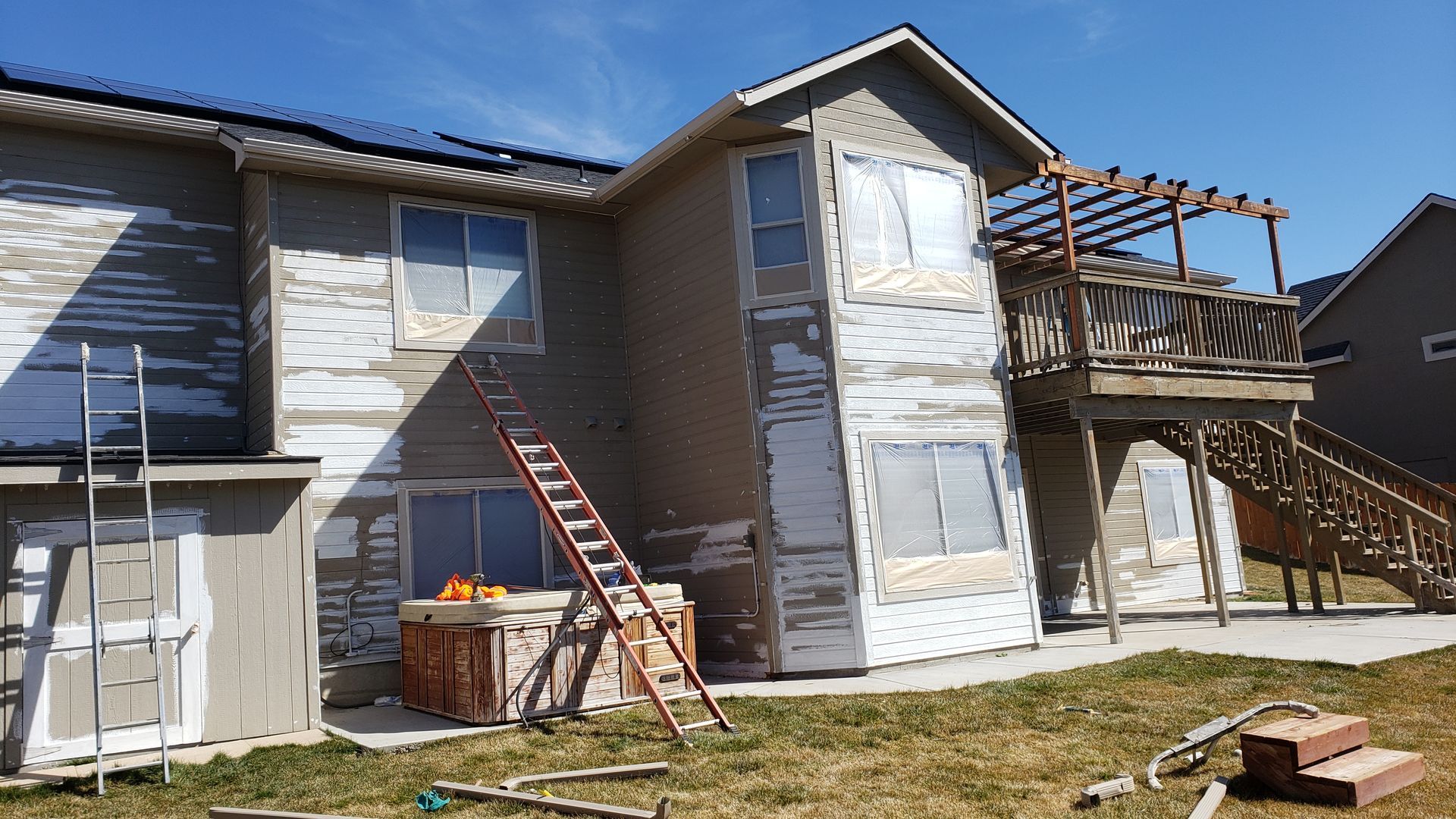 Two-story house with peeling paint, ladder, and partially covered windows; exterior undergoing renovation.