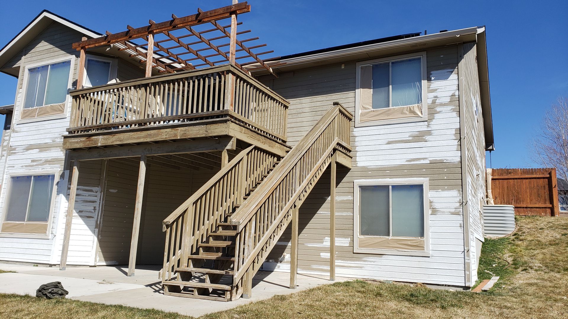 Back view of a two-story house with a wooden deck and stairs. The siding is weathered and some paint is peeling.