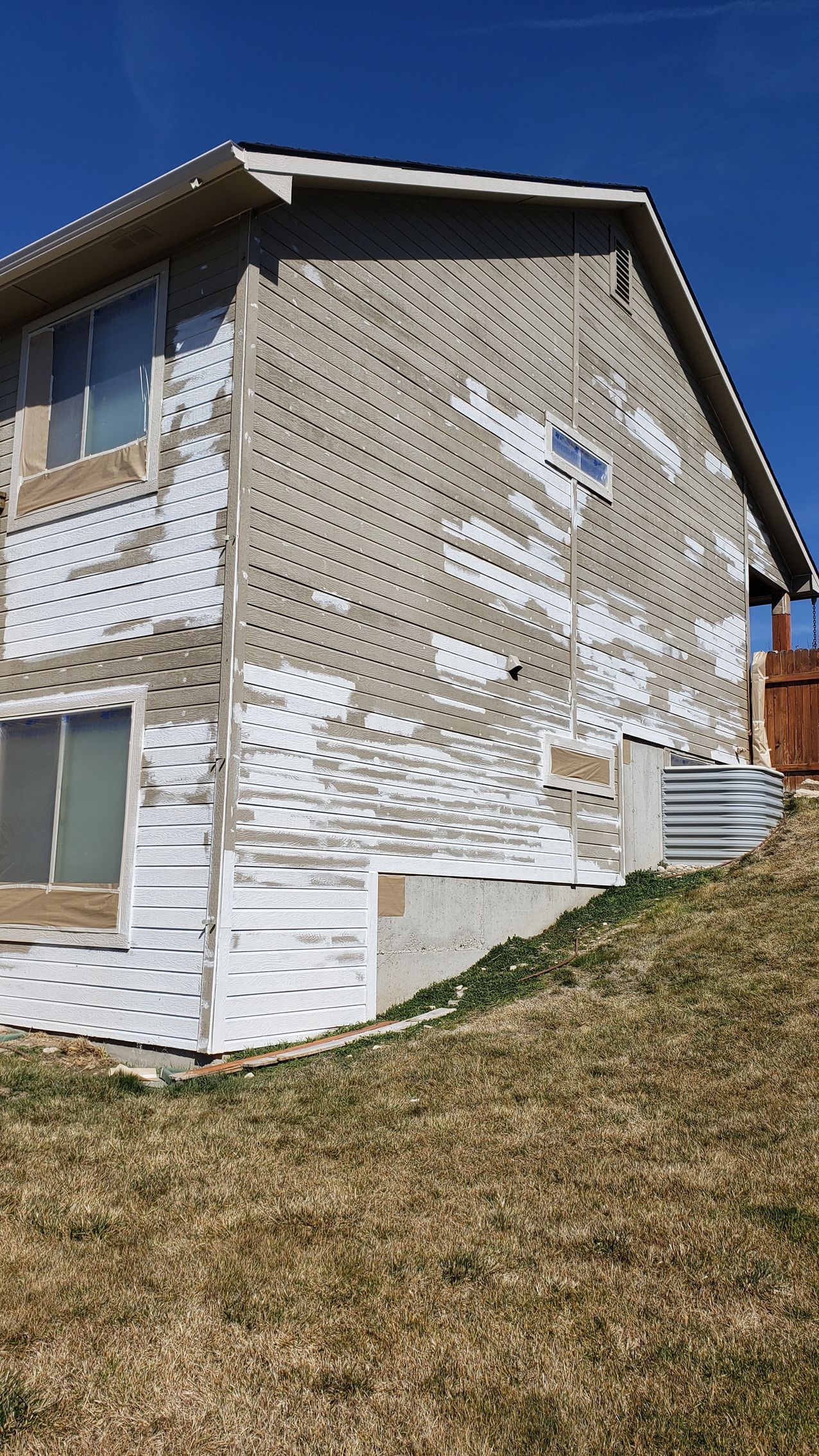 Side of a two-story building with exposed construction materials, including white wrap and gray siding under a clear blue sky.