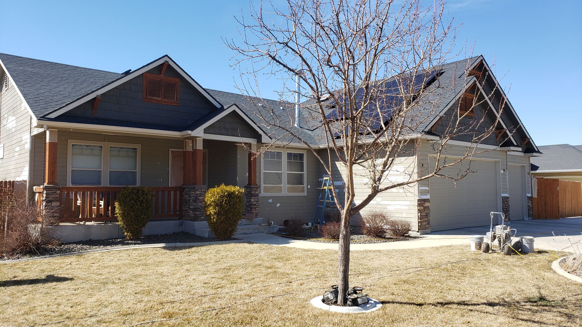 A light-colored house with a covered porch and a bare tree in front under a clear blue sky.