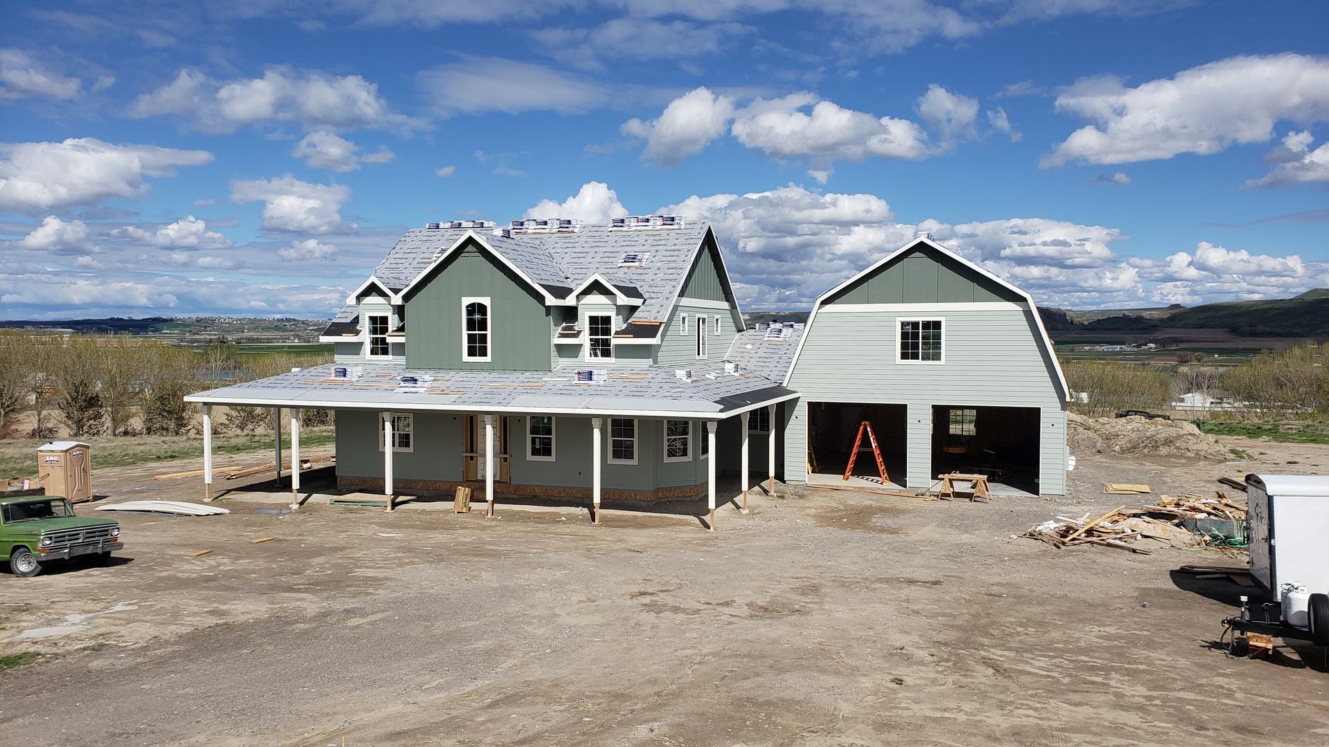 A two-story house under construction with a garage attached. The exterior is painted green with gray roofing.