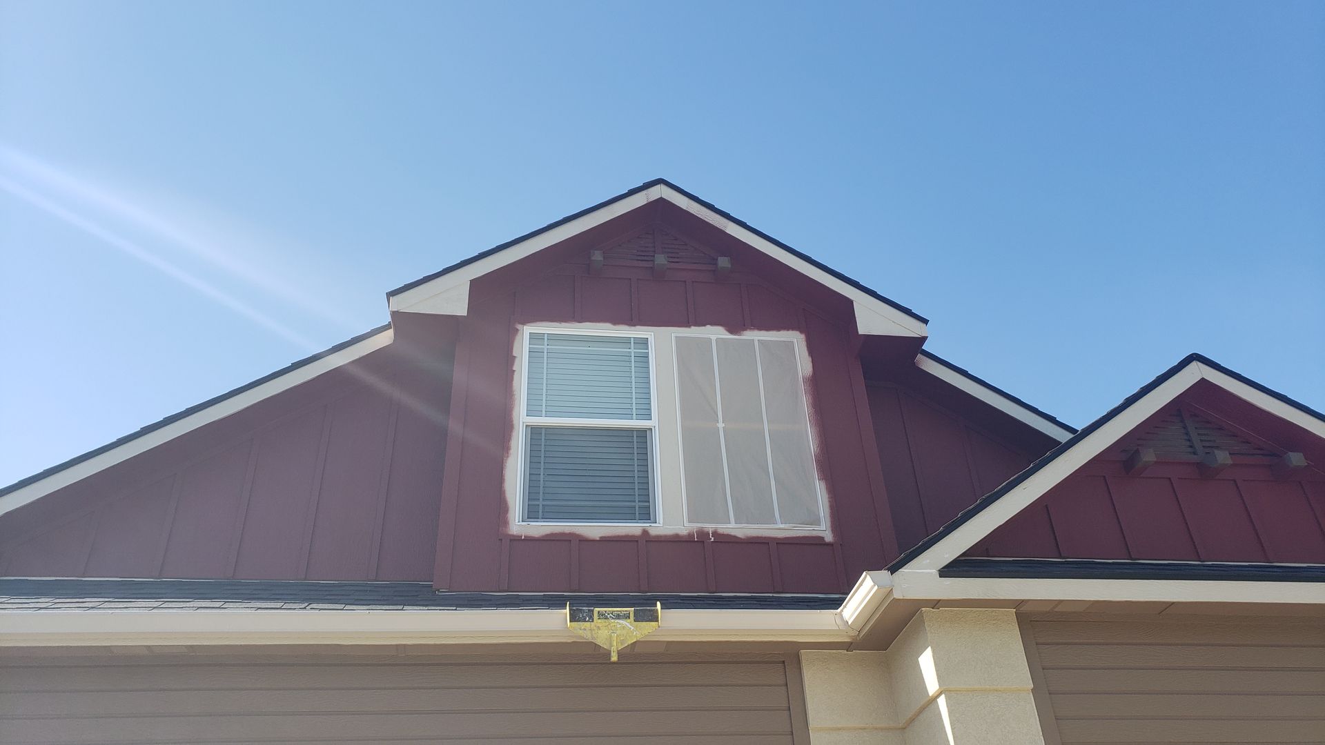 Red-sided house with a window covered in tape during what appears to be painting or construction. The sky is blue.