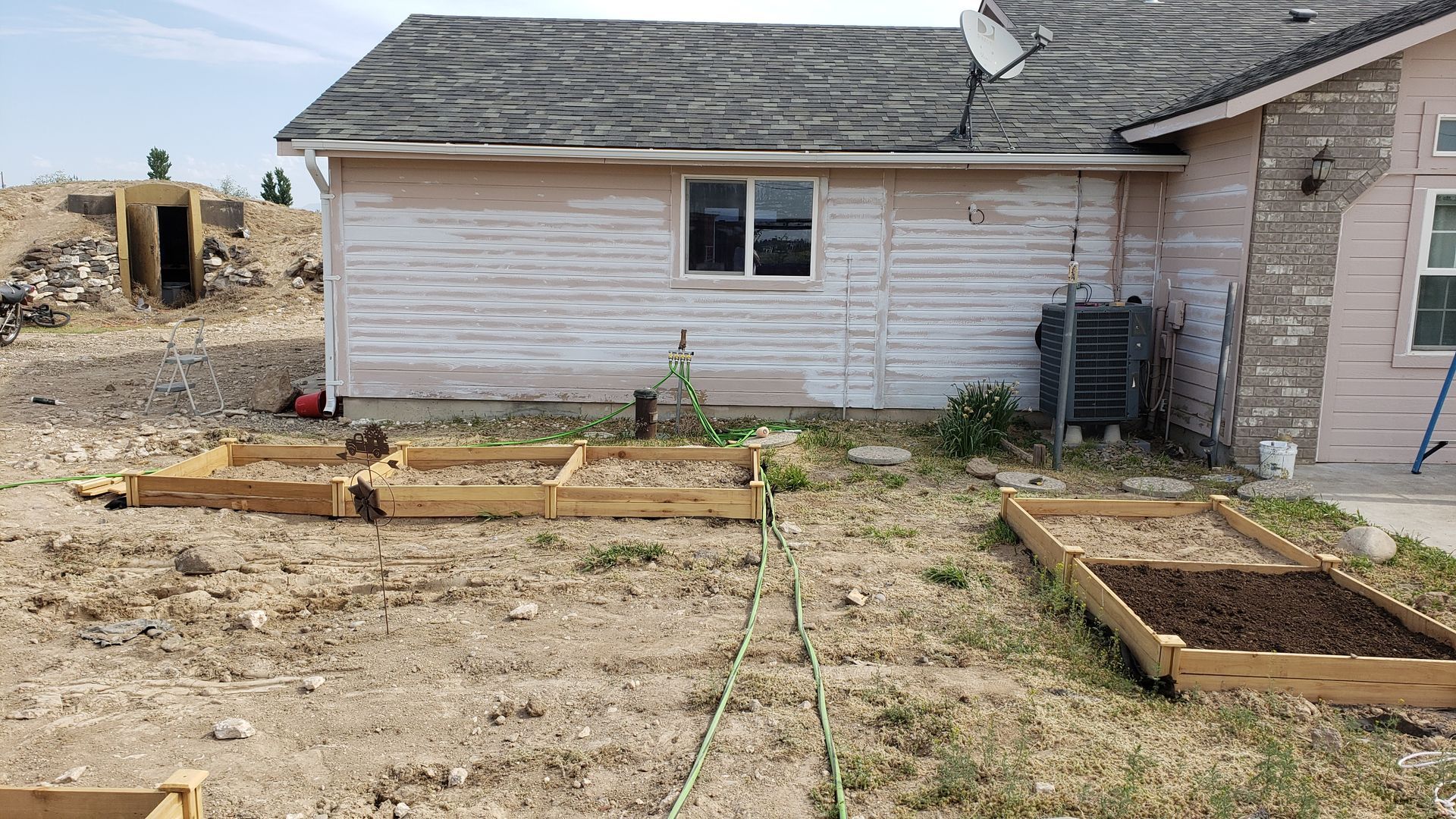 Backyard garden with several raised wooden beds, next to a house with weathered siding.