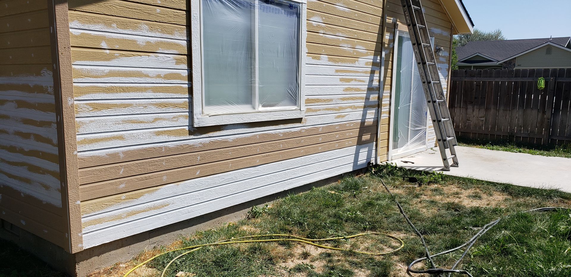 A house exterior with peeling paint and a ladder, grass and a sidewalk in the foreground.