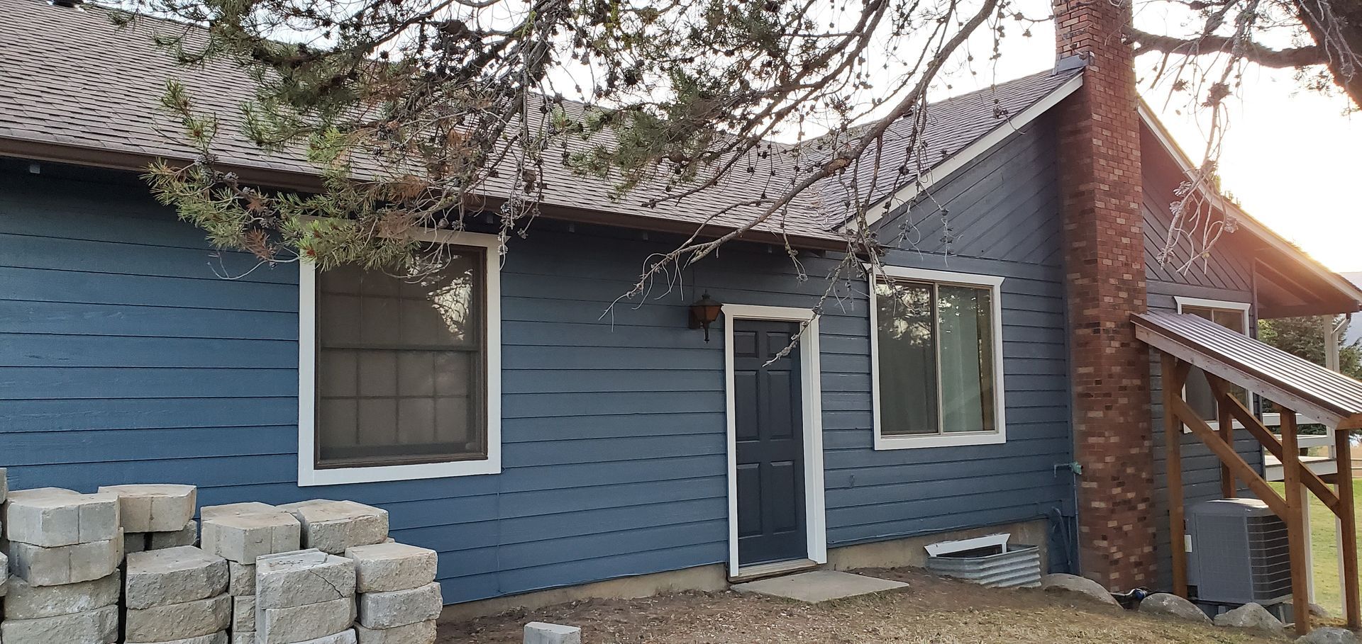 A blue house with a brick chimney and a dark door. Gray cinder blocks are stacked in the foreground.